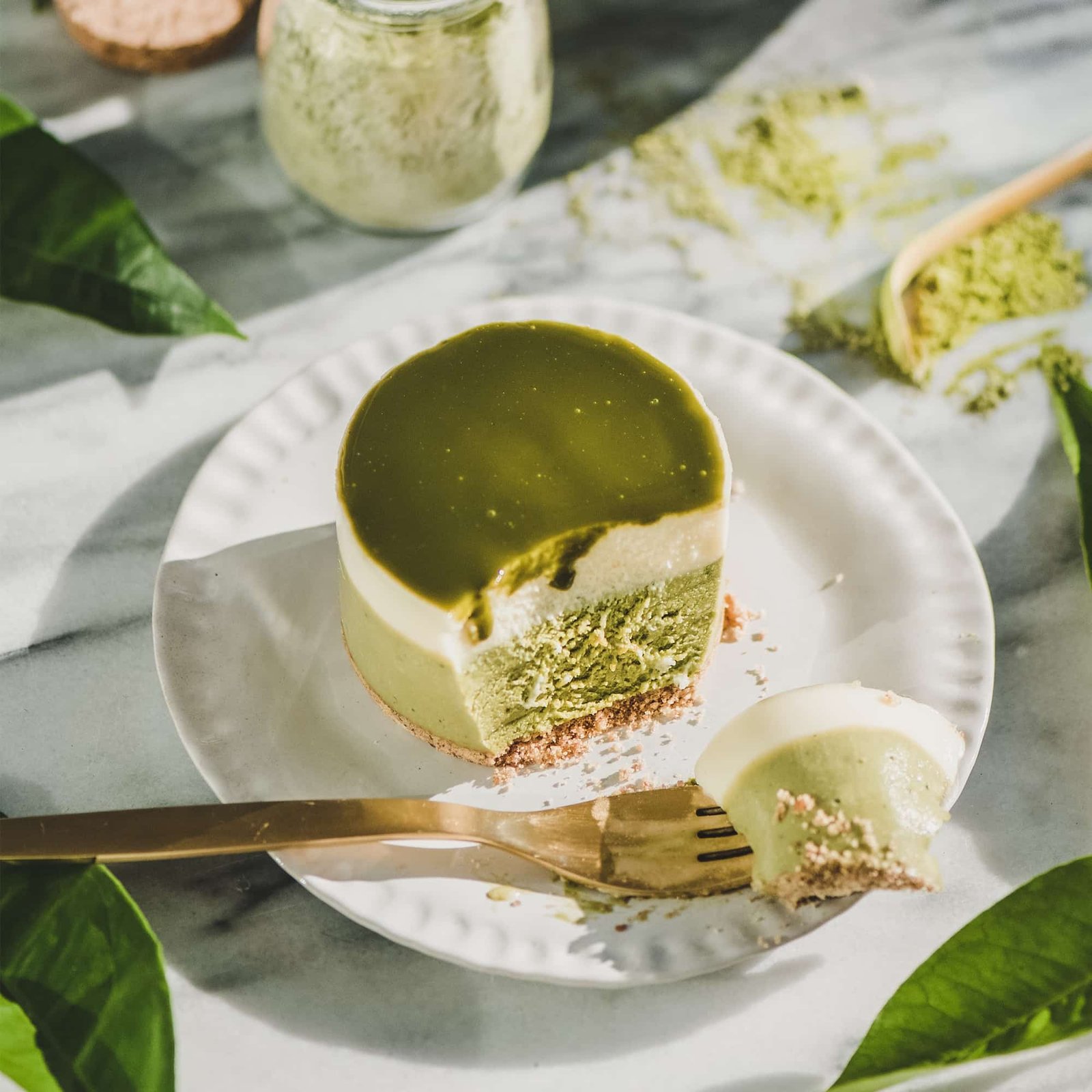Matcha cheesecake with glossy green glaze and a slice removed, served on a white plate with a gold fork