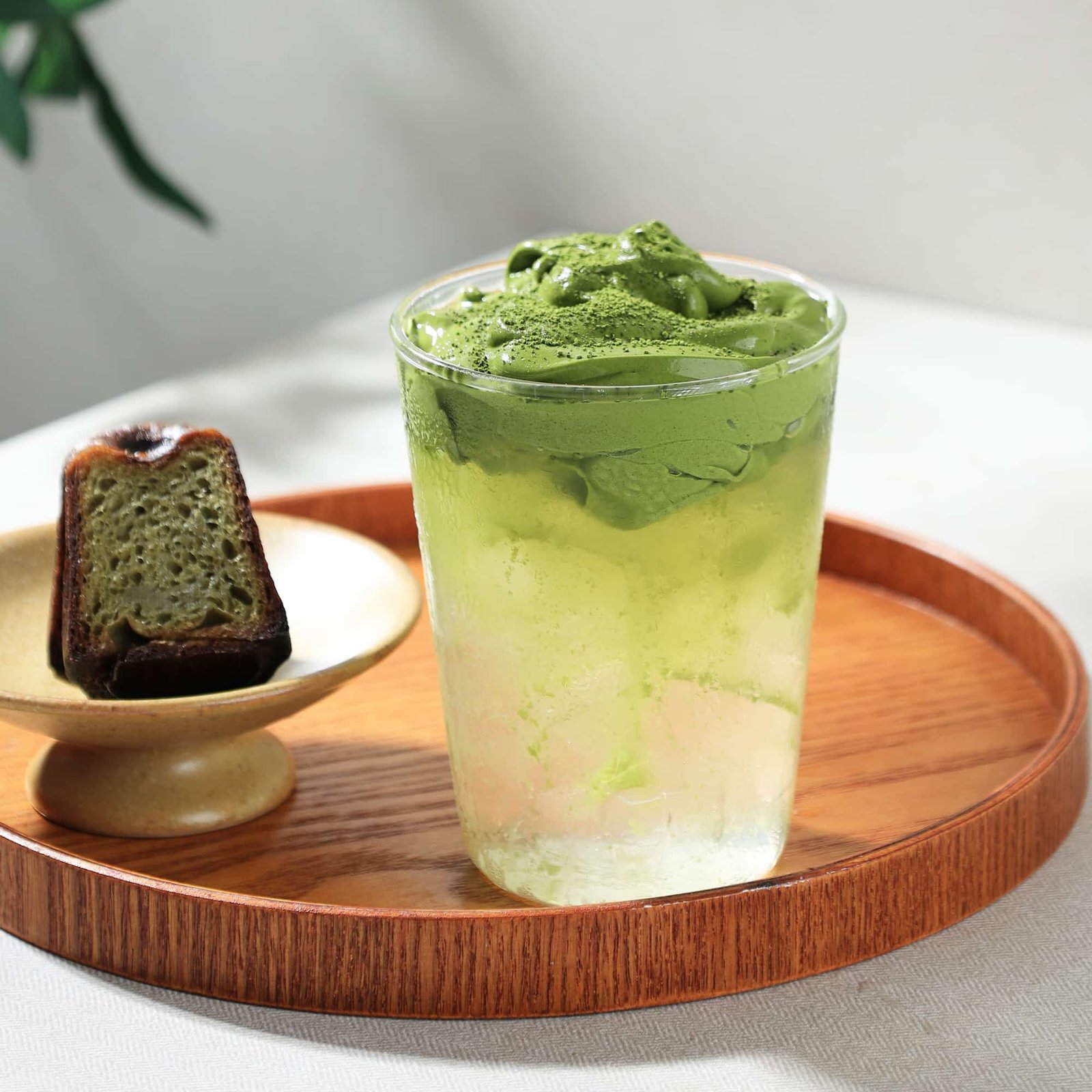 Iced matcha cloud beverage with layered milk and whipped matcha topping, served with a slice of matcha cake on a wooden tray