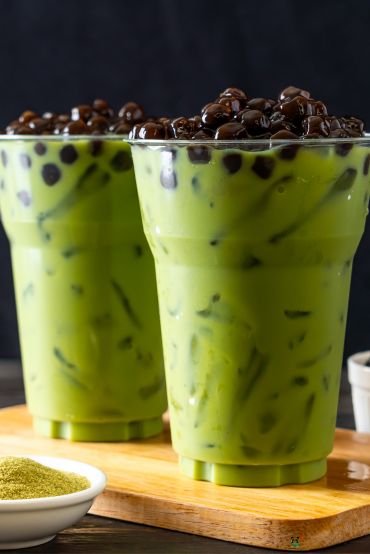 Two cups of iced matcha bubble tea with tapioca pearls on a wooden board